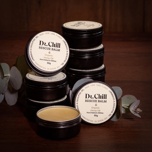 Dr. Chill Rescue Balm containers on a wooden surface with eucalyptus leaves.